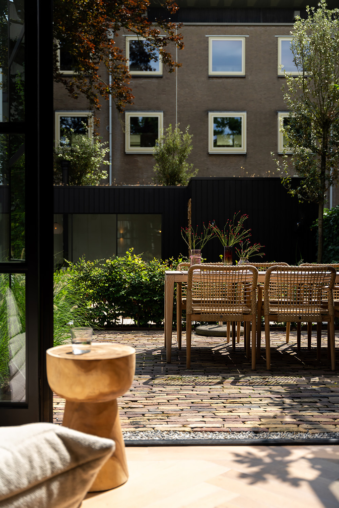 Lage drempel tussen de binnenvloer en een terras van gebakken klinkers met houten tuinstoelen